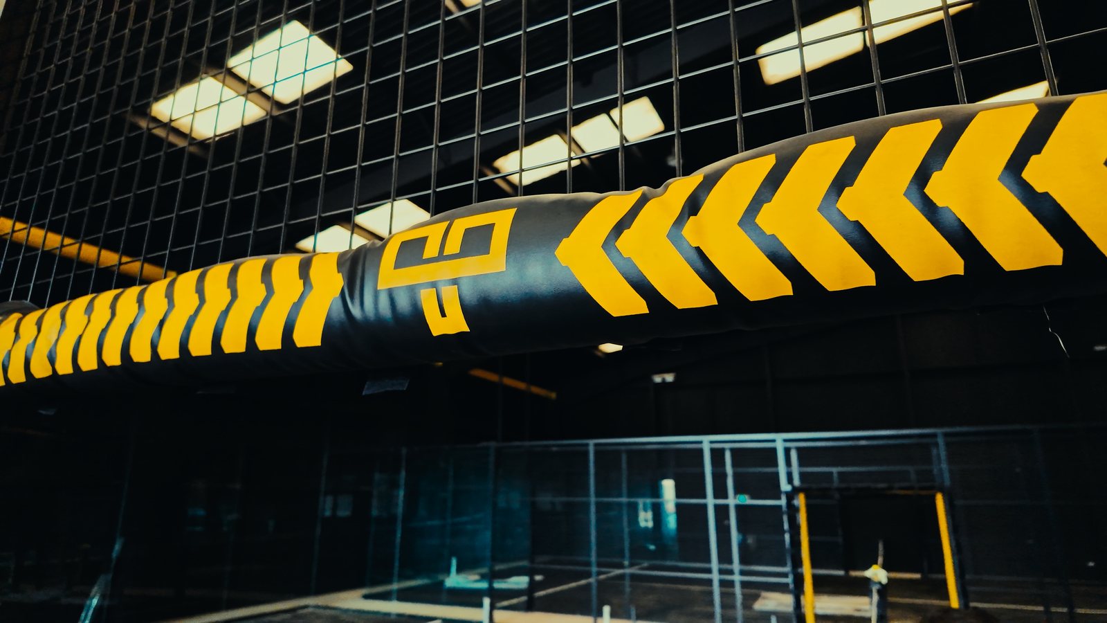 A padded court crossbar with amber chevron branding over a finished court, its glass and doors below