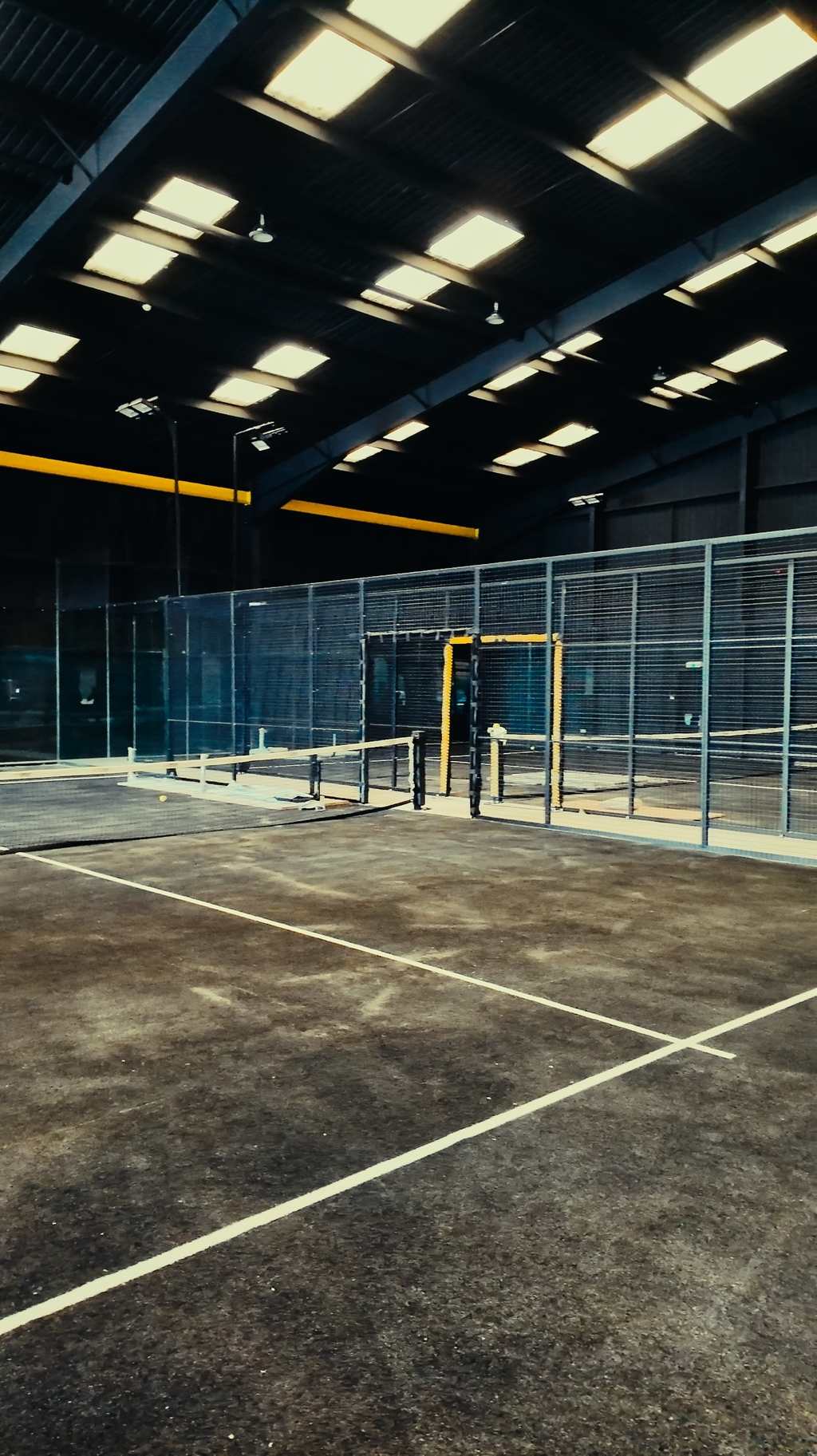 Looking into a padel court through its glass wall, with the facility lit behind