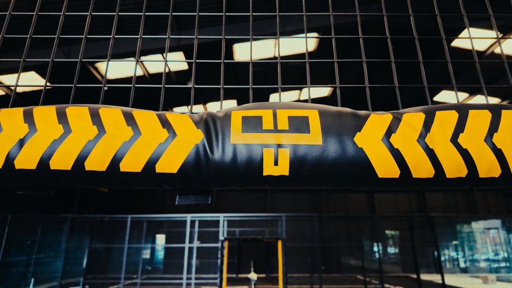 A padded court crossbar finished in black with yellow chevrons and a monogram.
