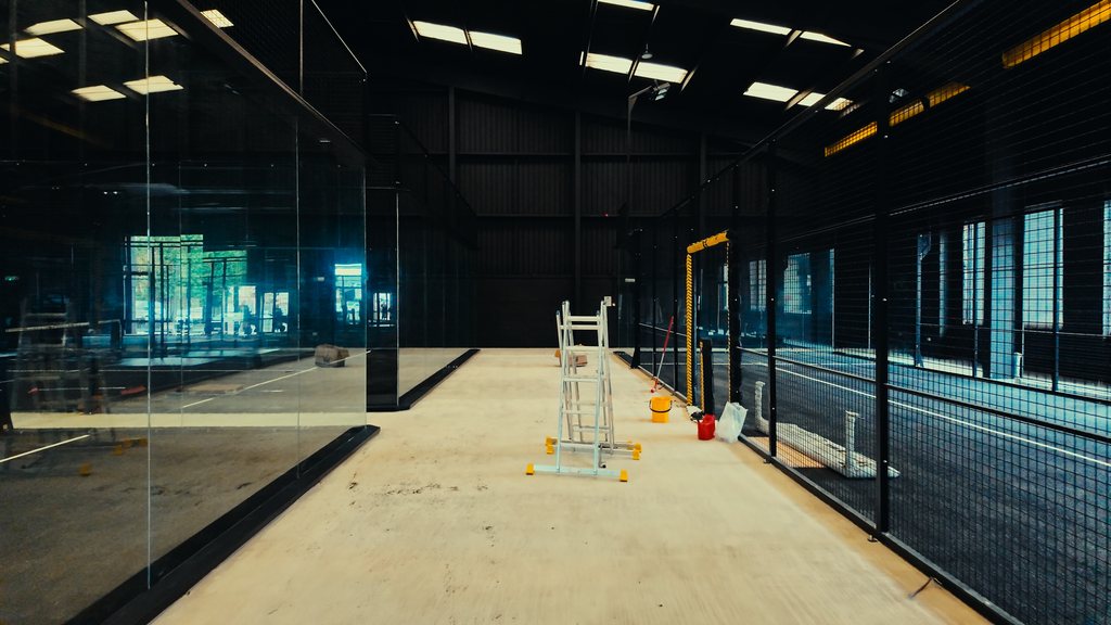 A padel court structure with tempered glass panels installed and the playing surface being prepared.
